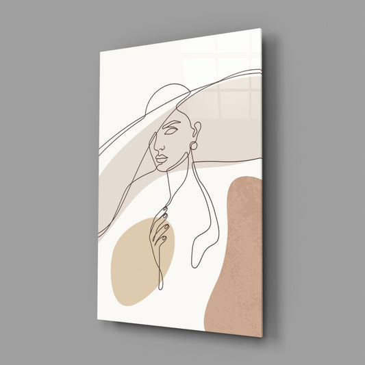 Glass wall art panel displaying line-drawn woman in wide-brimmed hat with beige and tan abstract shapes on white background, angled perspective view.