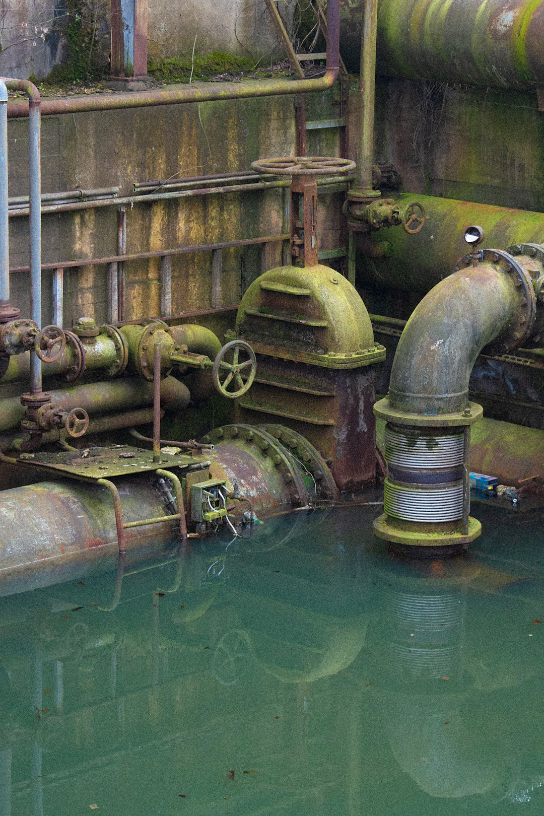 Abandoned industrial revolution water system with rusted pipes and valves in murky green water
