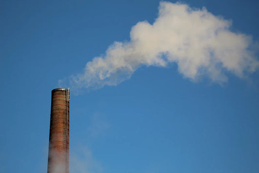 Brick industrial smokestack releasing white smoke, contributing to greenhouse gas emissions