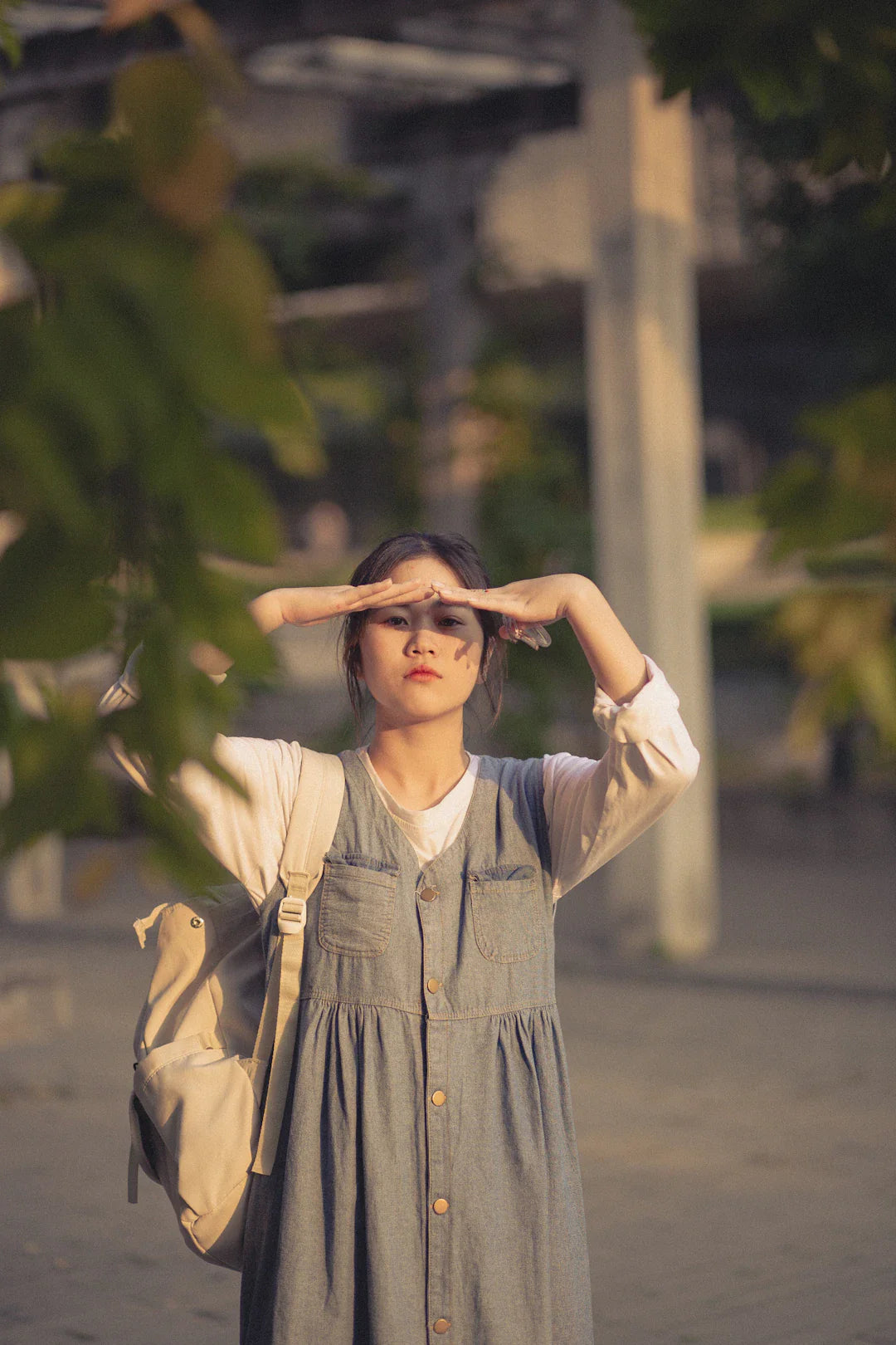 Young woman in denim dress shielding eyes, showcasing 90s photography influence on shaping personal branding
