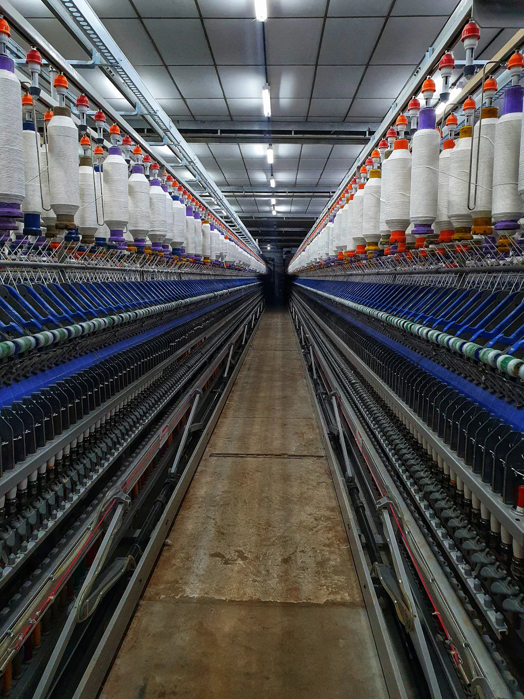 Long corridor of textile machinery with white thread spools in Northeast mills