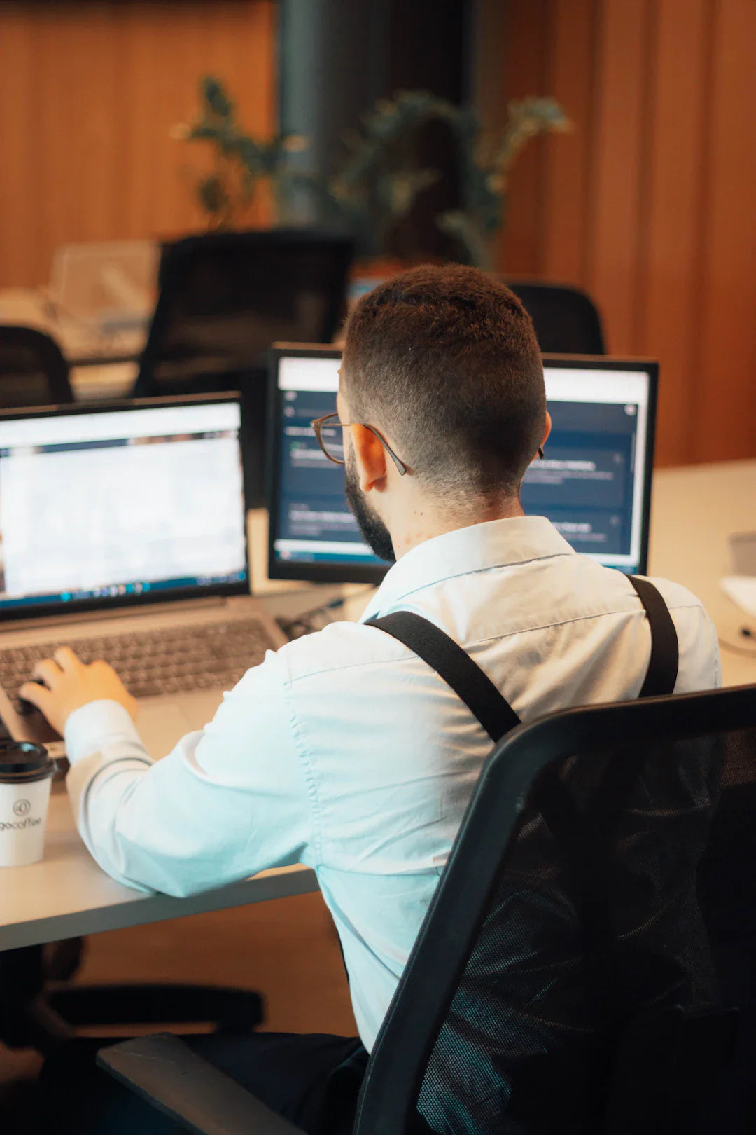 Man in white shirt and suspenders using AI on dual monitors