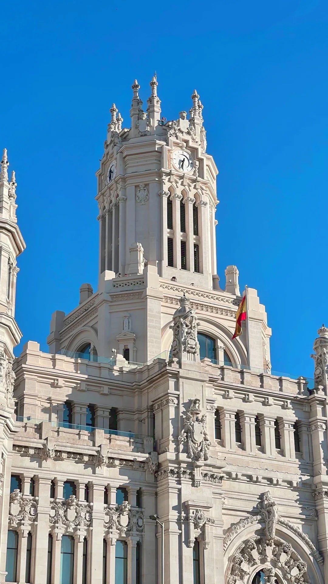 White stone building with clock tower and Spanish flag, showcasing automobile revolution