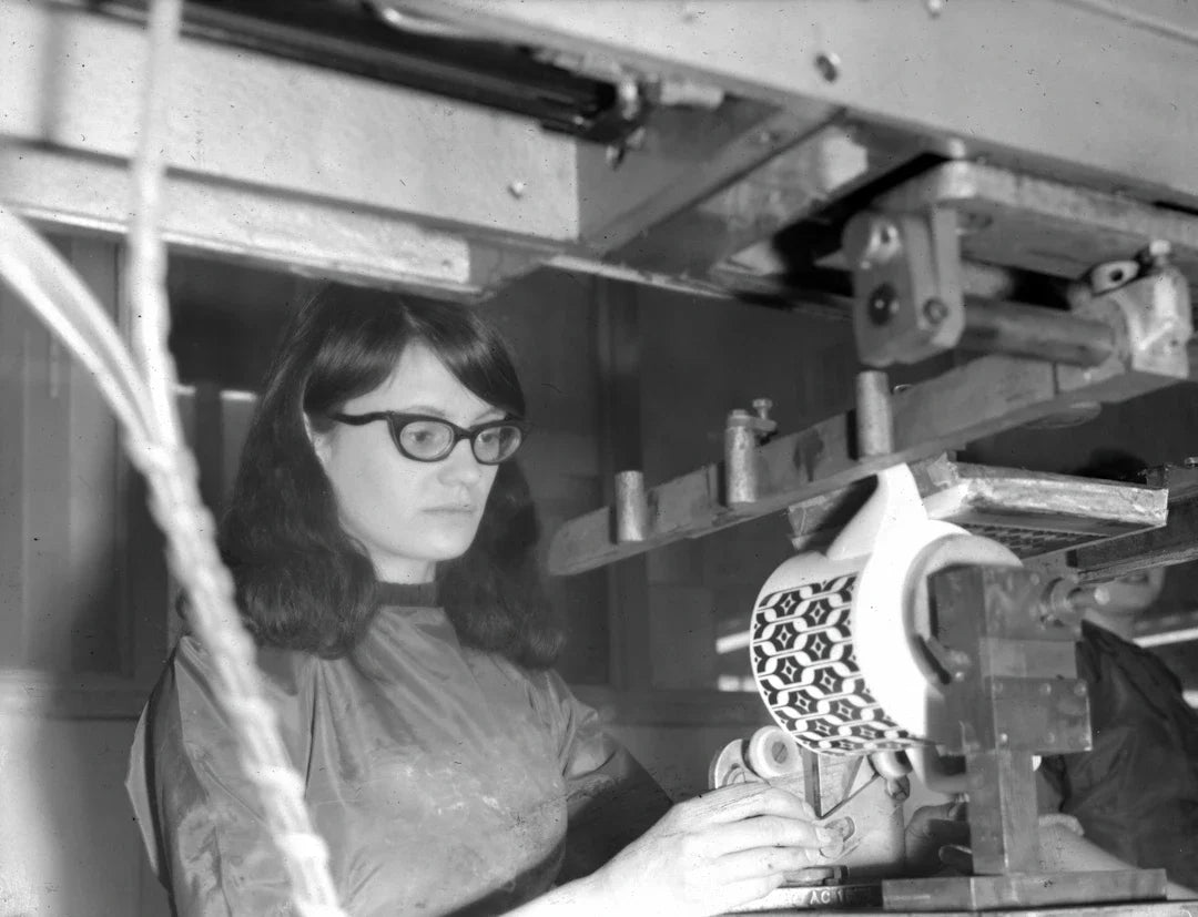 Woman with dark hair and glasses decorating patterned object during industrial revolution labor efforts