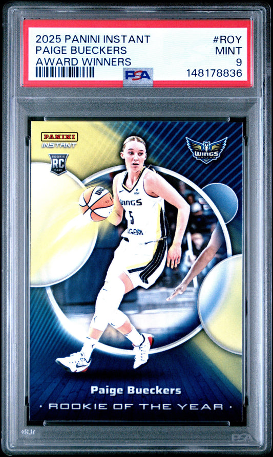 Front view of graded basketball card in plastic case showing Paige Bueckers in white Wings uniform dribbling basketball.