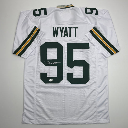 White Green Bay Packers jersey number 95 with "WYATT" nameplate and autographed signature, displayed flat lay against gray background.