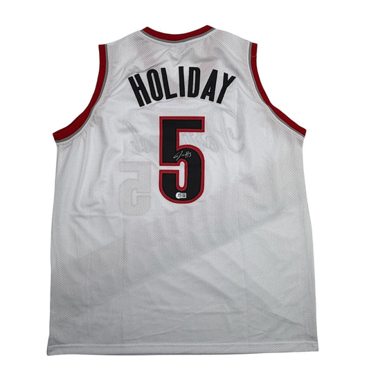 Back view of white mesh basketball jersey with red trim, displaying "HOLIDAY" and number "5" with signature and authentication badge.