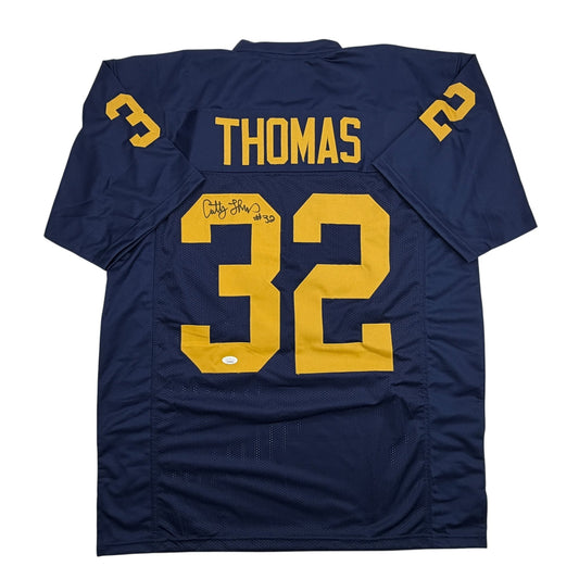 Back view of navy blue Michigan football jersey number 32 with gold lettering reading "THOMAS," featuring an autographed signature.
