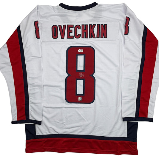 Back view of white hockey jersey with red and navy trim, displaying "OVECHKIN" and number 8 in red with navy outline, signed in blue marker.