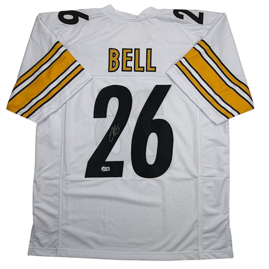 White Pittsburgh Steelers football jersey number 26 with "BELL" nameplate, signed, displayed flat showing front and sleeves with yellow and black stripes.