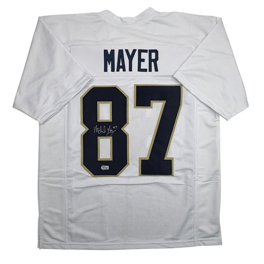 White Notre Dame football jersey displaying "MAYER" nameplate and number "87" with gold and navy trim, signed, laid flat.