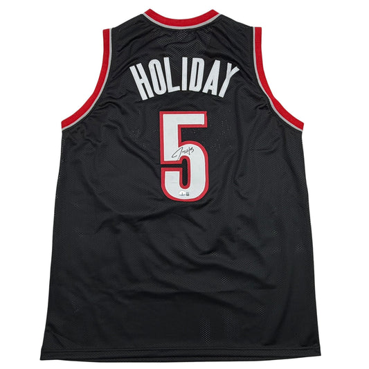 Back view of black mesh basketball jersey with red trim displaying "HOLIDAY" and number "5" with autograph.