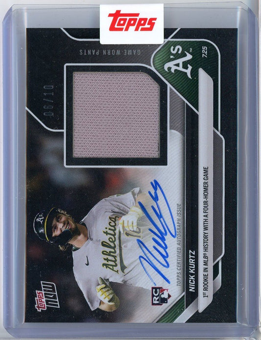 Front of baseball card showing Nick Kurtz in white Athletics uniform with blue autograph, gray fabric swatch, and black background with card numbering.