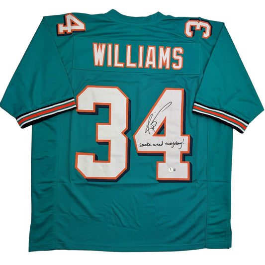 Teal Miami Dolphins football jersey number 34 with "Williams" nameplate, signed with "Smoke weed everyday" inscription, displayed flat on white background.