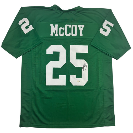 Green football jersey with white "McCoy" nameplate and number 25, displayed flat against white background, front view showing autograph on chest number.