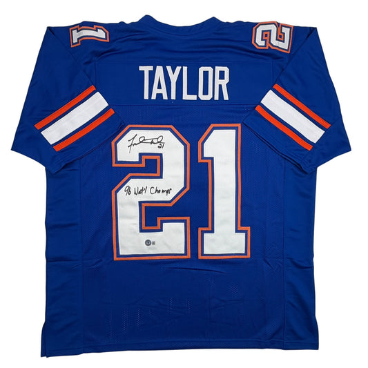 Blue college football jersey with "TAYLOR" and number 21 displayed, signed with "96 Natl Champ" inscription, flat lay front view.