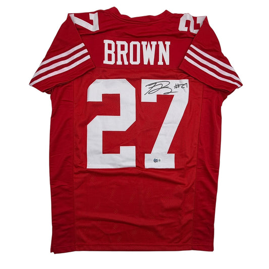 Red San Francisco 49ers football jersey #27 with "BROWN" nameplate and autographed signature, flat lay front view.