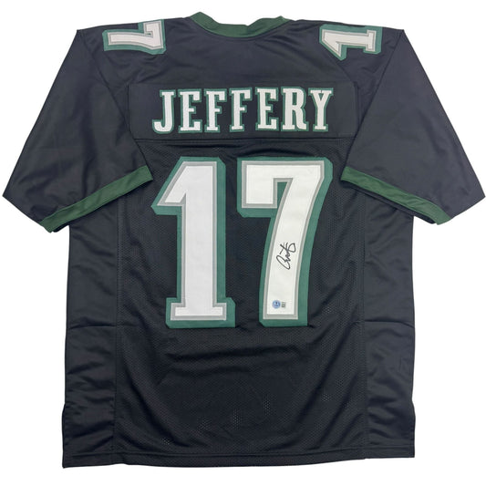 Back view of black football jersey with green and white trim displaying "JEFFERY" and number "17" with autograph.