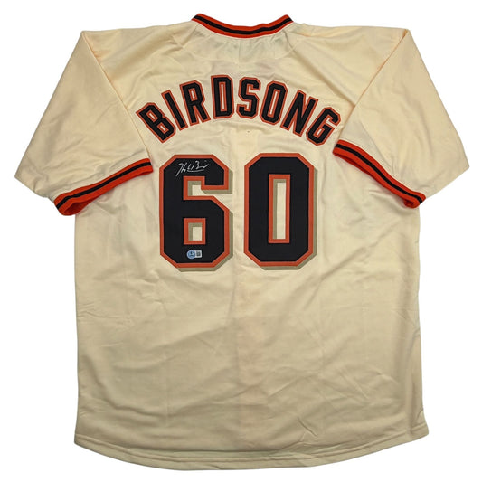 Back view of cream-colored baseball jersey with "BIRDSONG" and number "60" in black and red, signed above the number.
