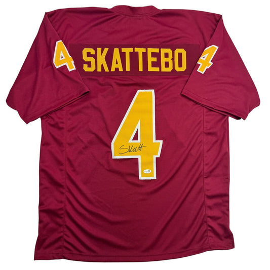 Back view of maroon college football jersey with yellow number 4, "SKATTEBO" text, and autographed signature.