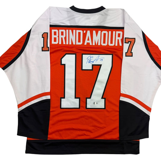 Back view of red, white, and black hockey jersey with "BRIND'AMOUR" and number 17 with handwritten signature.