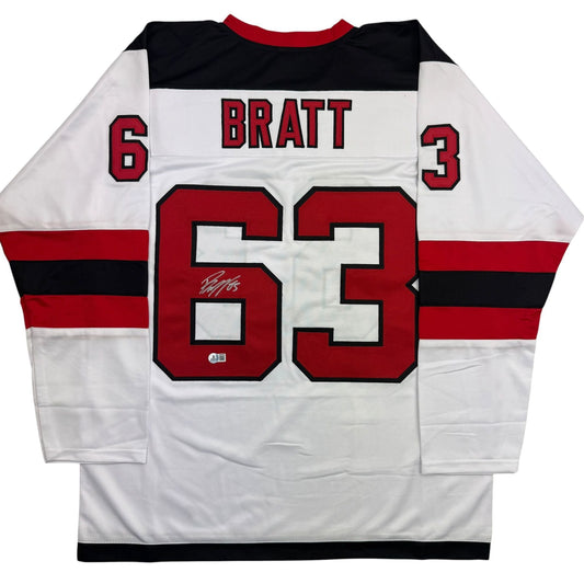 Back view of white hockey jersey with red and black horizontal stripes, displaying "BRATT" and number 63 with autograph.