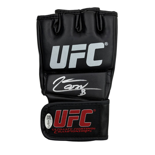 Black UFC MMA fighting glove with white logo, silver signature, and red text on wrist cuff, displayed flat against white background.