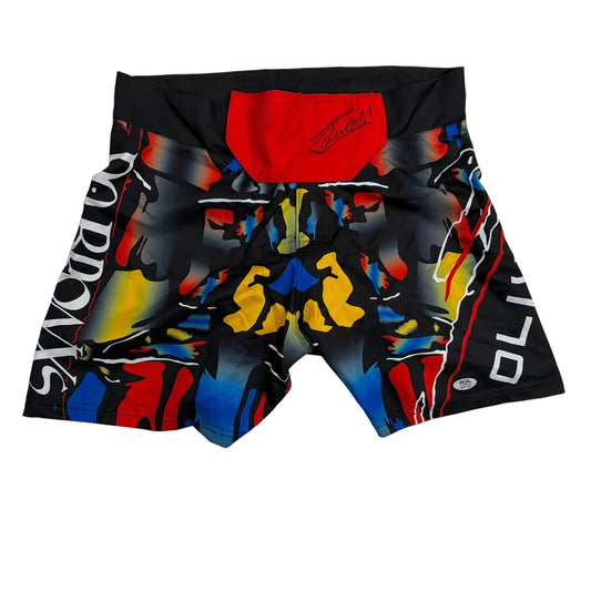 Black MMA fighting shorts with red waistband, colorful abstract design in red, yellow, and blue, displayed flat lay view.