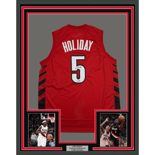 Red Portland Trail Blazers basketball jersey number 5 with "HOLIDAY" name and autograph, displayed in frame with two accompanying player photographs.