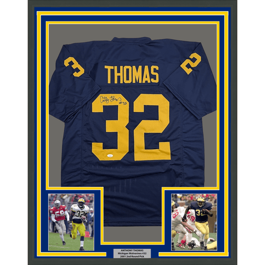 Navy blue football jersey number 32 with "THOMAS" and yellow lettering, signed, displayed in frame with yellow and blue borders and two action photos below.