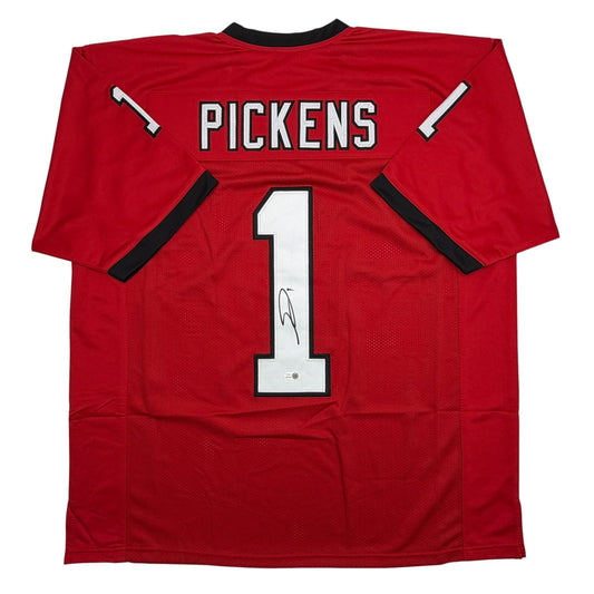 Back view of red Georgia college football jersey with "PICKENS" and number "1" in white, featuring black shoulder stripes and visible autograph on the number.