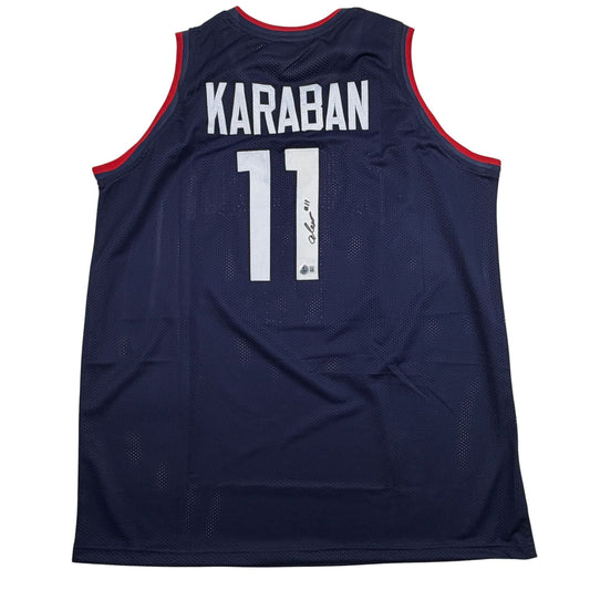 Back view of navy blue mesh basketball jersey with red trim, white "KARABAN 11" text, and autographed signature on number.