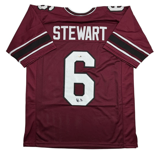 Maroon college football jersey with white number 6 and "STEWART" nameplate, flat lay front view showing mesh fabric and black sleeve stripes.