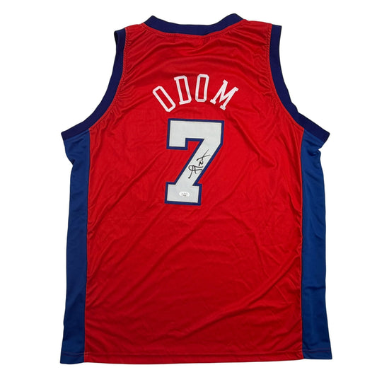 Back view of red and navy basketball jersey displaying "ODOM" and number 7 with signature on white number.
