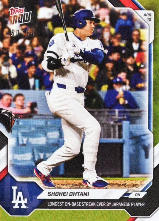 Shohei Ohtani mid-swing in white Dodgers uniform, blue helmet, crowd blurred behind, Topps Now card with gold foil border and stat text.