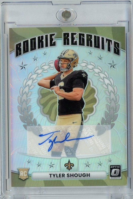 Front of graded rookie football card showing Tyler Shough in black Saints jersey with gold helmet, blue autograph, and holographic refractor background.