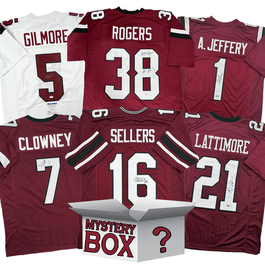 Six autographed maroon and white college football jerseys arranged around a white mystery box, displaying player names Gilmore, Rogers, Jeffery, Clowney, Sellers, and Lattimore.