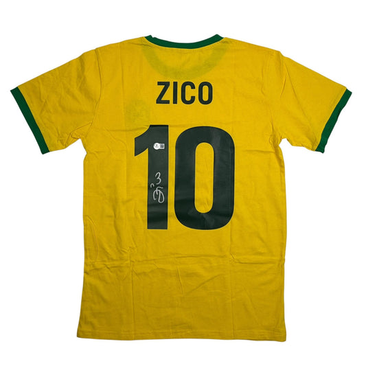 Back view of yellow Brazil soccer jersey with green trim, displaying "ZICO" and number 10 with handwritten autograph.