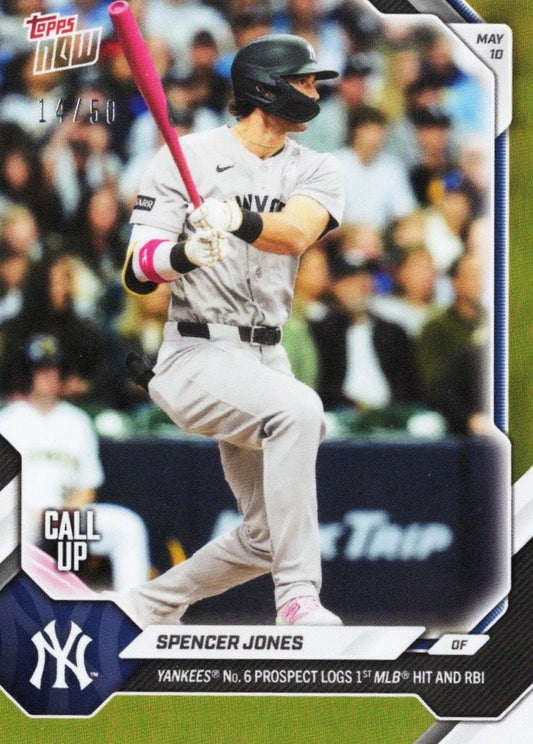 Spencer Jones in batting stance wearing gray Yankees uniform with pink bat and accents, mid-swing during game with blurred crowd background.