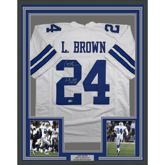 Framed white Dallas Cowboys jersey number 24 signed by Larry Brown, displayed with two action photographs and nameplate in blue and white matting.