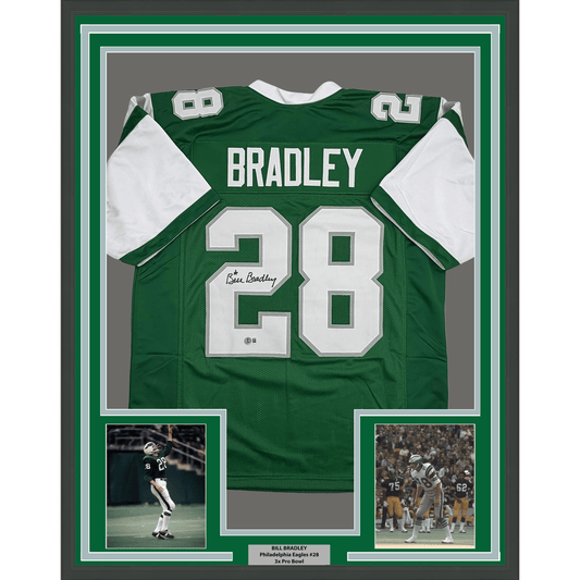 Framed green Philadelphia Eagles jersey number 28 signed by Bill Bradley, displayed with two action photographs and authentication plaque.