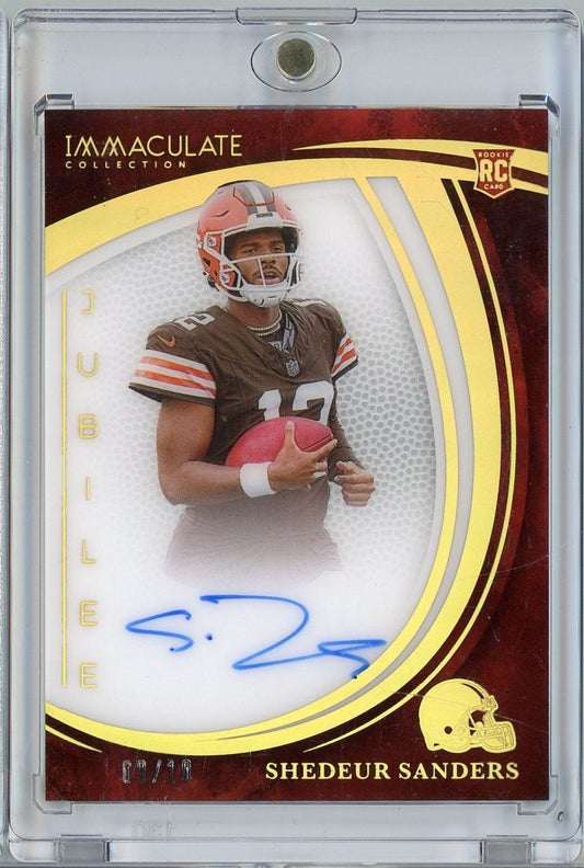 Signed rookie football card in clear plastic case showing Shedeur Sanders in brown Cleveland Browns uniform holding red football.