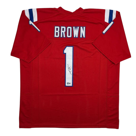 Red New England Patriots football jersey with "BROWN" nameplate and number "1" on back, displayed flat with visible autograph on number.