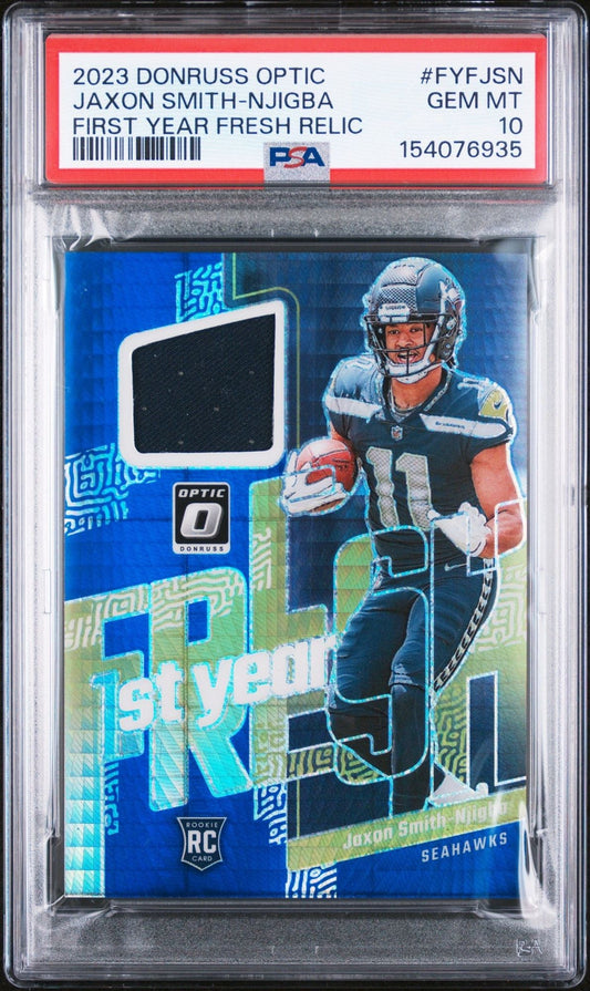 PSA-graded trading card in clear holder showing Jaxon Smith-Njigba in Seahawks uniform on blue background with relic swatch window and "1st Year" text.