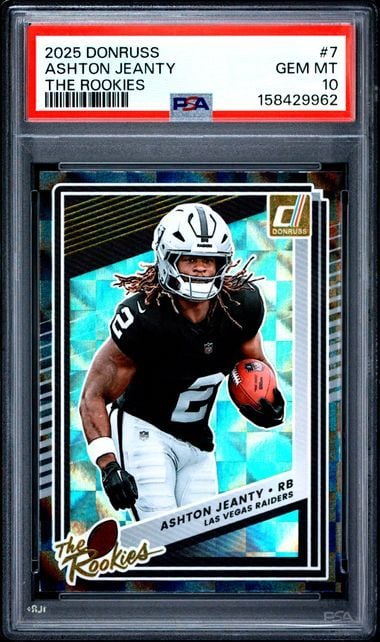 PSA-graded rookie football card in clear case showing Ashton Jeanty in black Raiders uniform holding red football against cyan geometric background.