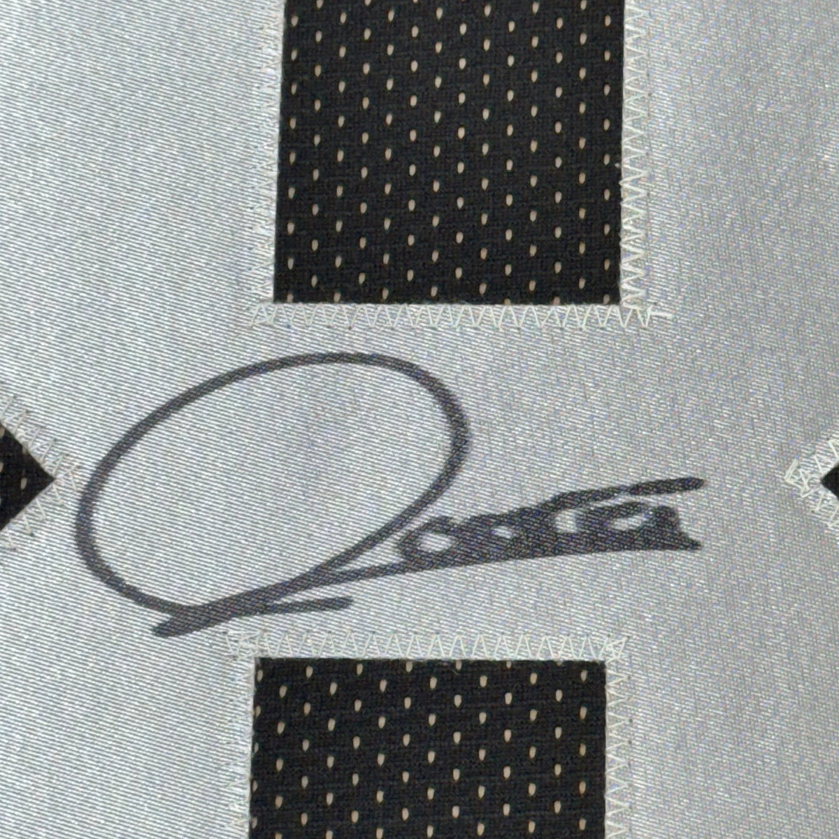 Close-up of a black ink signature with a looping oval on grey jersey fabric, between black perforated mesh panels.