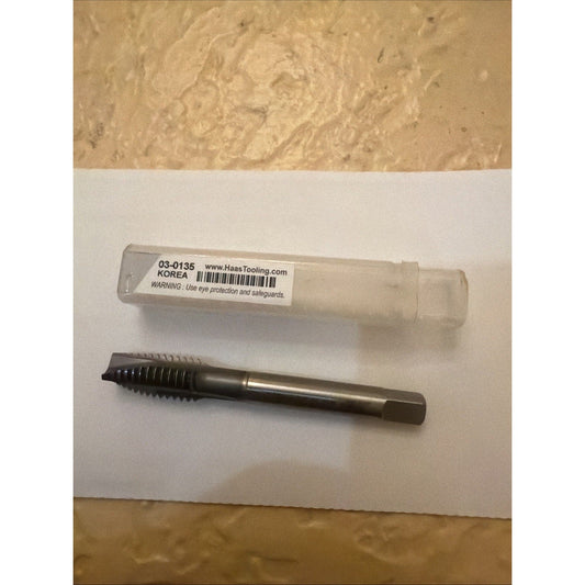 Haas spiral flute tap 03-0135 in transparent plastic case beside metal threading tool on white background.