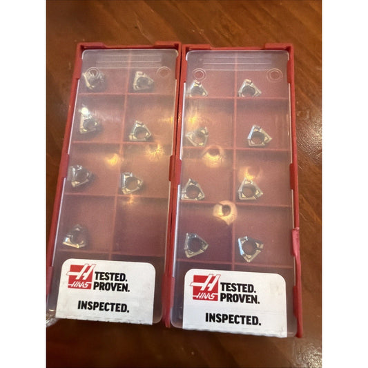 Two red Haas compartment boxes containing triangular carbide inserts with white "Tested. Proven. Inspected." labels visible on wooden surface.