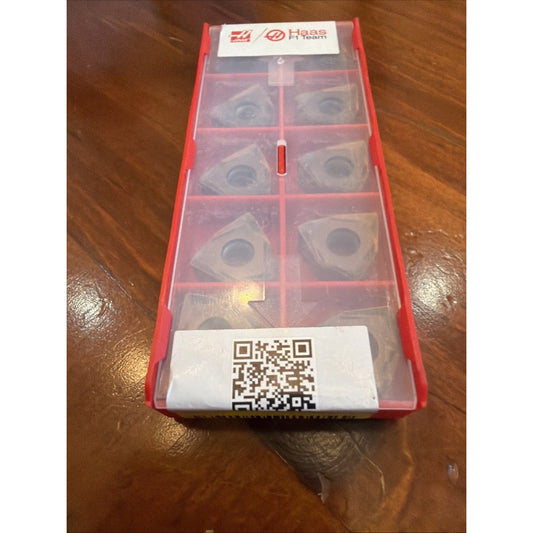 Red plastic case with ten compartments containing metallic carbide inserts, Haas Team branding visible, QR code on bottom label.