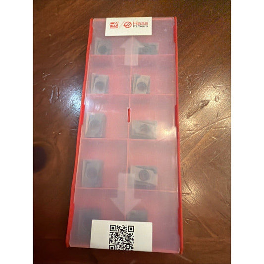 Red plastic case containing multiple carbide insert compartments, labeled with Haas F1 Team logo and QR code, viewed from above.